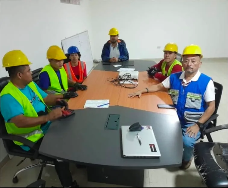 Reunión de varias personas con cascos y chalecos alrededor de una mesa.