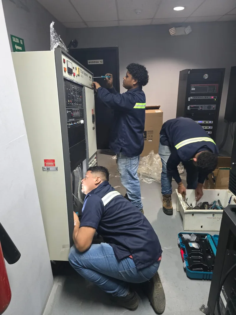 Tres técnicos con uniforme institucional desmontando un gabinete de equipos en una sala técnica, con herramienta desplegada.