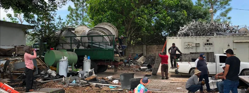 Operación de desmontaje y clasificación en El Salvador: equipo numeroso trabajando, camión cargado con estructuras metálicas y acopio de material.